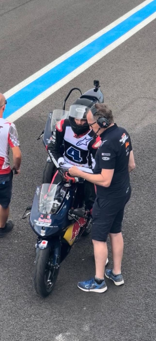 Josh on a Red Bull bike in the pit lane, wearing number 4, as a team member goes through a sheet with him.