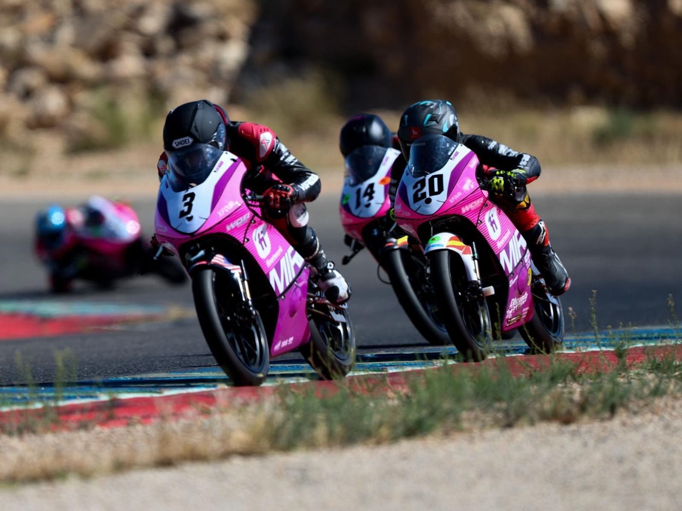 Josh, number 3 with a US flag on the fairing, leading two riders through a corner on pink MIR bikes.