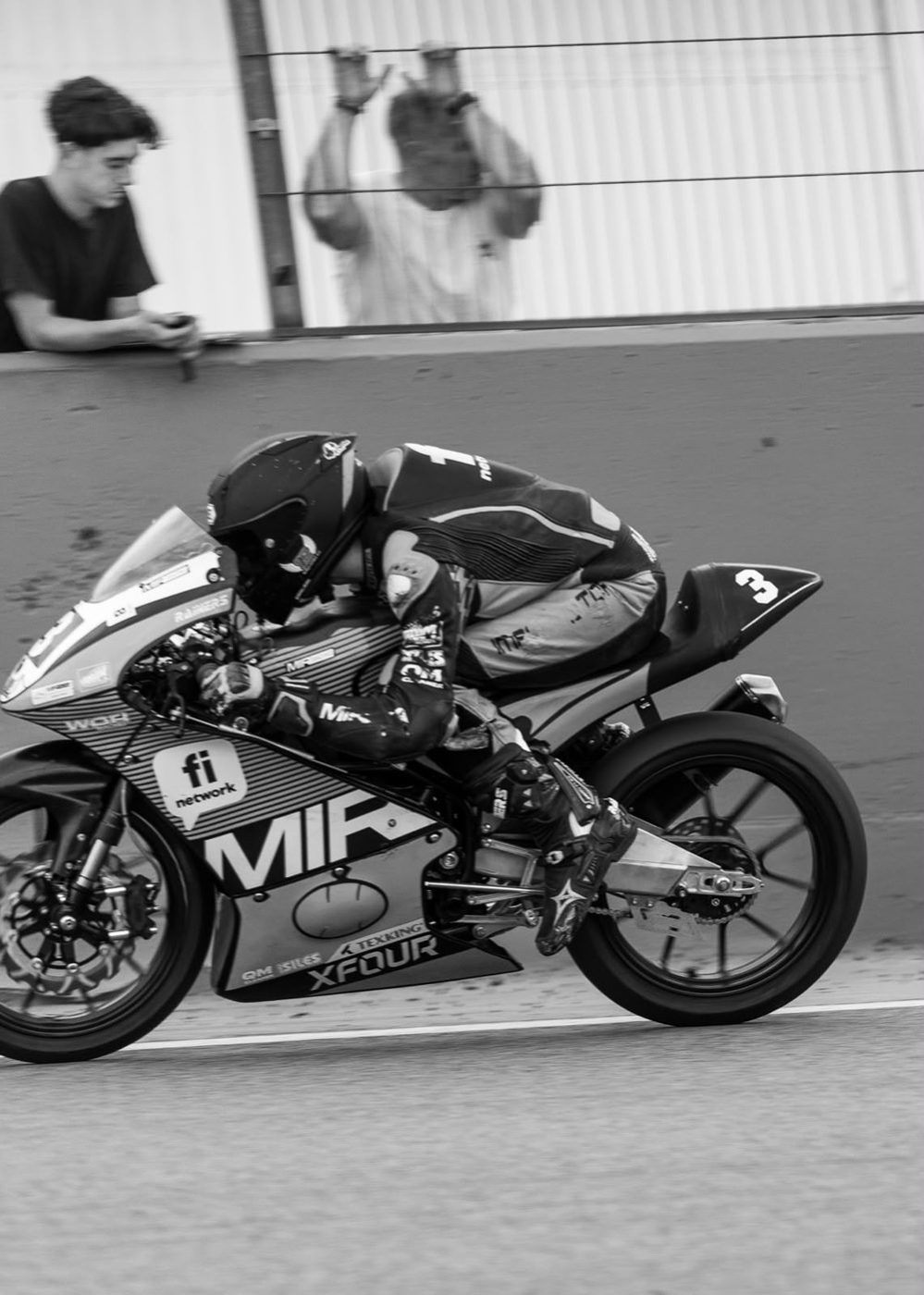 Josh at speed on the MIR bike in black and white, tucked in along a pit wall.